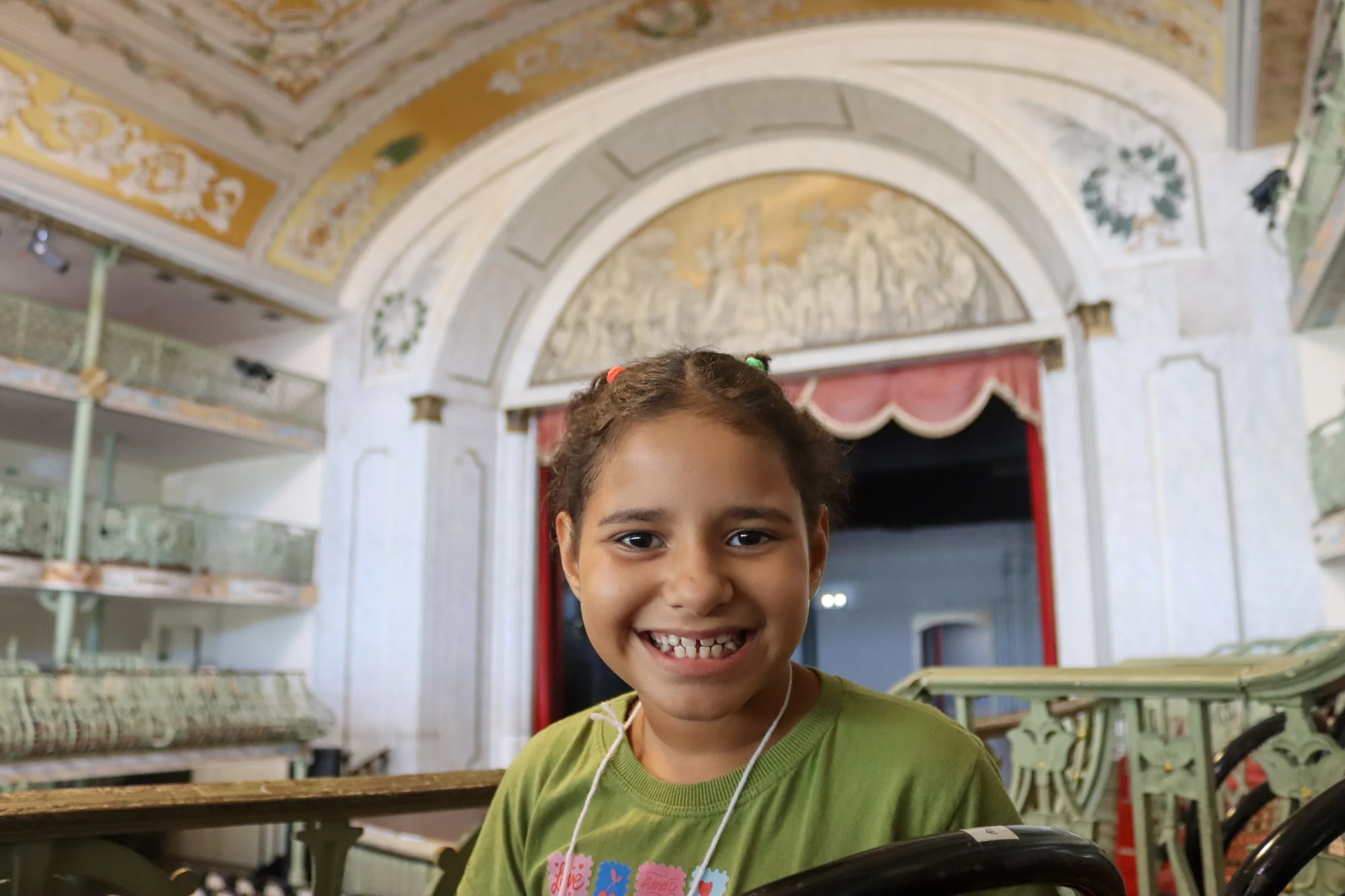 Menina de camiseta verde sorrindo em um ambiente ornamentado