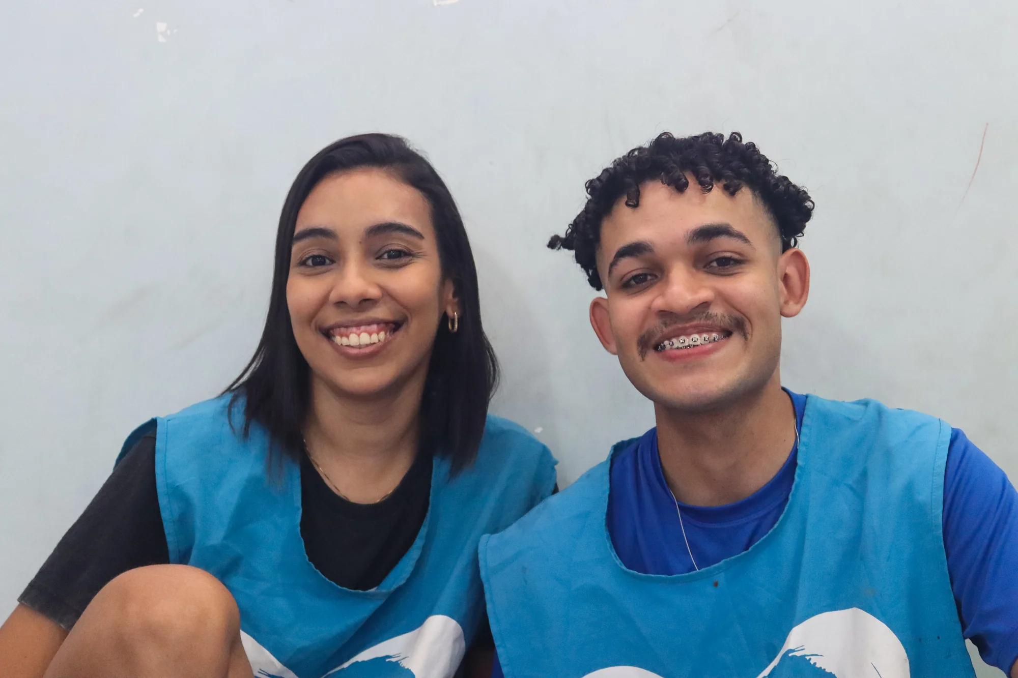 Duas pessoas sorrindo lado a lado, vestindo coletes azuis